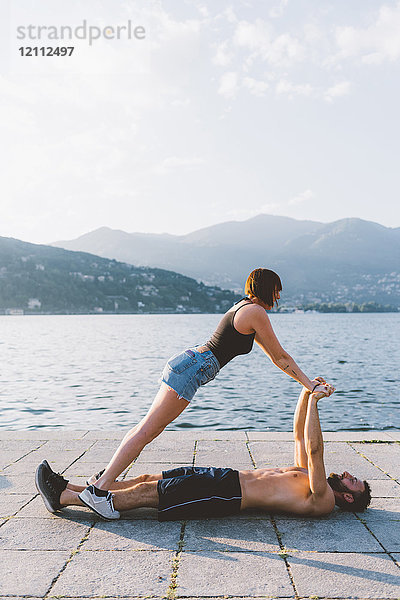 Junge Frau balanciert mit ihrem am Wasser liegenden Freund  Comer See  Lombardei  Italien