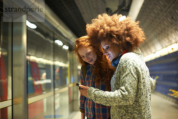 Zwei junge Frauen am Bahnhof mit Blick auf ein Smartphone
