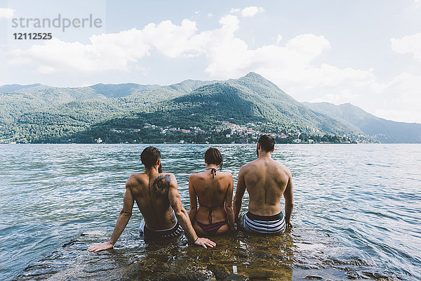 Rückansicht von drei jungen erwachsenen Freunden  die am Comer See sitzen  Como  Lombardei  Italien