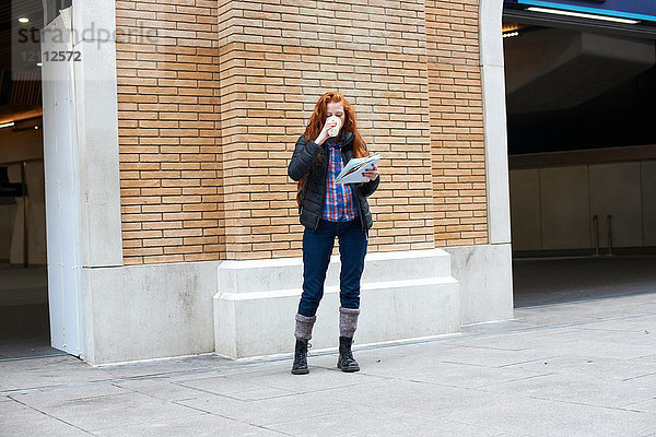 Junge Frau steht auf der Straße  trinkt Kaffee  hält Karte