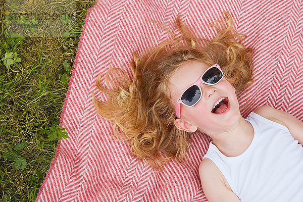Kopfporträt eines Mädchens mit blonden Haaren und Sonnenbrille  das auf einer Decke posiert