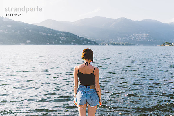 Rückansicht einer jungen Frau am Wasser mit Blick auf den Comer See  Lombardei  Italien