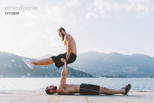 Auf dem Rücken liegender junger Mann unterstützt Freund am Wasser  Comer See  Lombardei  Italien