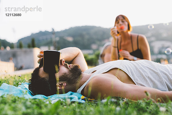 Junger Mann liegt im Gras und schaut durch ein Virtual-Reality-Headset  Como  Lombardei  Italien