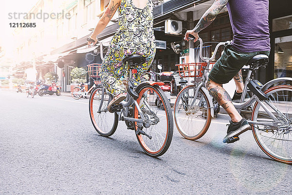 Taillenansicht eines multiethnischen Hipster-Paares  das mit dem Fahrrad die Straße entlang fährt  Schanghai Französische Konzession  Schanghai  China