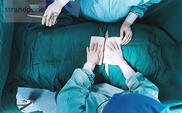 Draufsicht auf Chirurgen  die im Operationssaal der Entbindungsstation eine Operation am Abdomen durchführen