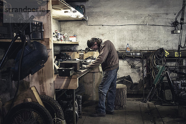 Mechaniker bei der Arbeit an der Werkbank mit zerlegtem Oldtimer-Motorrad in der Werkstatt