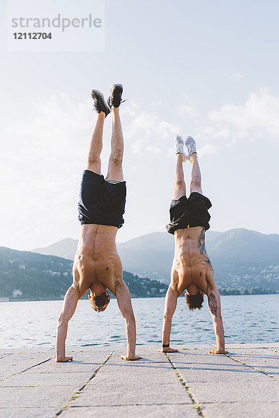 Zwei junge Männer machen Handstand am Wasser  Comer See  Lombardei  Italien