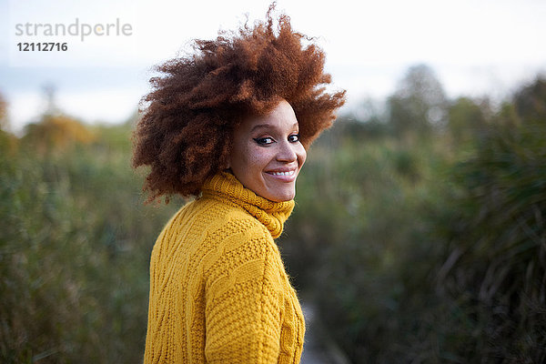 Porträt einer Frau mit Afro  die über die Schulter schaut und lächelnd in die Kamera blickt