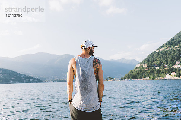 Rückansicht eines jungen Hipster-Männchens  das vom Wasser aus schaut  Comer See  Lombardei  Italien