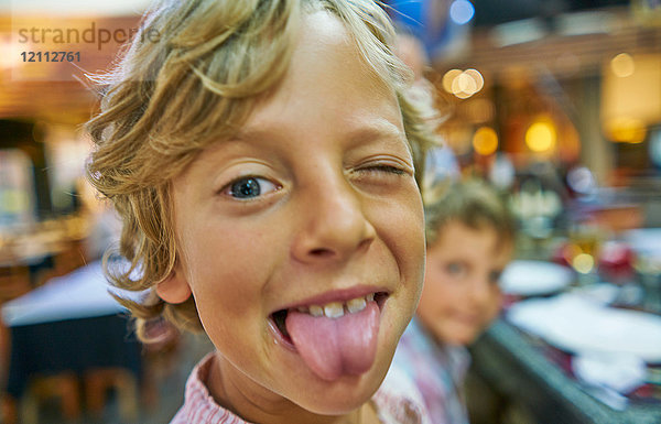 Porträt eines Jungen  der in die Kamera schaut und seine Zunge herausstreckt