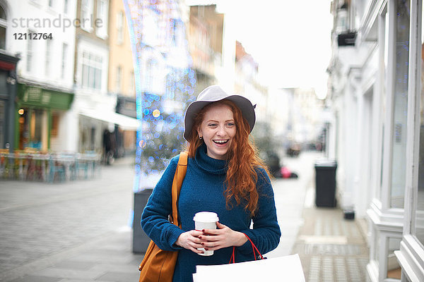 Junge Frau geht auf der Straße  hält Kaffeetasse und Einkaufstasche