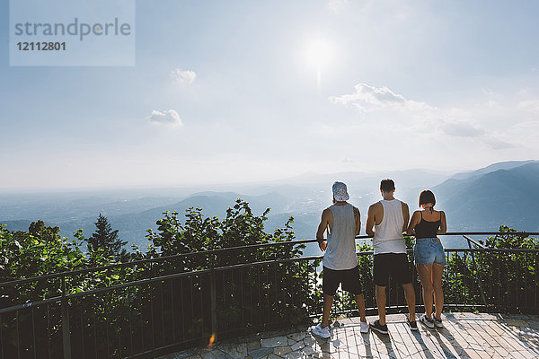 Rückansicht von drei jungen erwachsenen Freunden  die vom Balkon auf den Comer See blicken  Como  Lombardei  Italien