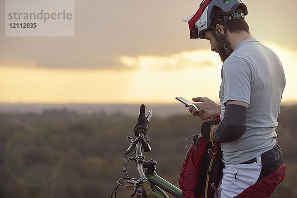 Männlicher Mountainbiker betrachtet Smartphone-Moorlandschaft