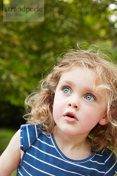 Porträt eines blonden  gewellten Mädchens mit blauen Augen  das in einen Park blickt