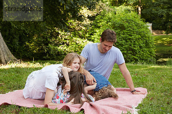 Mittlere erwachsene Eltern mit zwei Töchtern  die sich auf einer Picknickdecke im Park vorbeugen