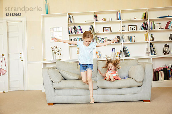 Zwei junge Schwestern springen vom Sofa und hüpfen auf dem Sofa