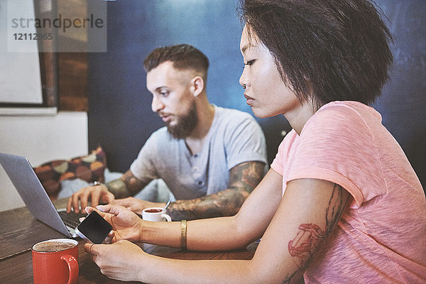 Multiethnisches Hipster-Paar im Café  das sich Smartphone und Laptop ansieht  Shanghai French Concession  Shanghai  China