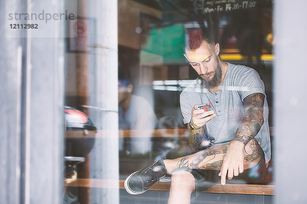 Junger männlicher Hipster im Fensterplatz eines Cafés mit Blick auf ein Smartphone  Shanghai French Concession  Shanghai  China