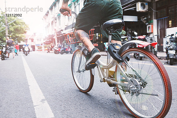 Taille eines jungen männlichen Hipsters  der mit dem Fahrrad die Stadtstraße entlang fährt  Shanghai French Concession  Shanghai  China