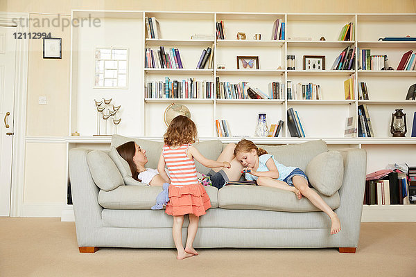 Frau auf Sofa liegend  während Töchter Märchenbuch lesen