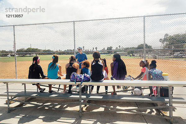 Männlicher Lehrer unterweist Schulmädchen-Fussballspieler auf der Sportplatzbank der Schule