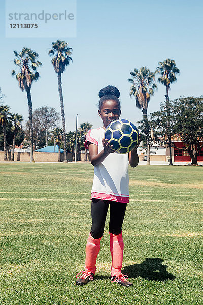 Porträt einer Schulfussballspielerin  die einen Fussball auf dem Schulsportplatz hält