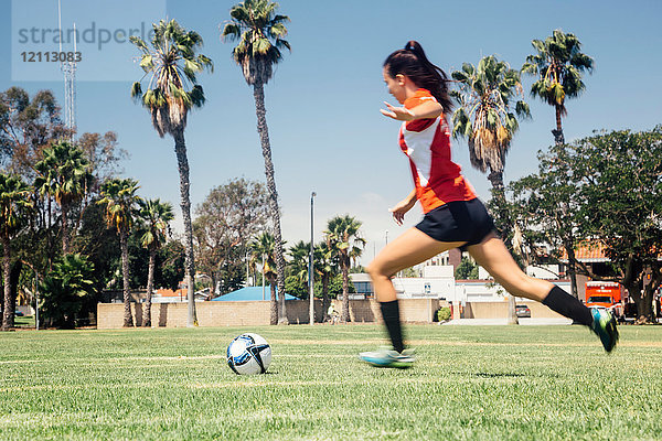 Teenager-Schülerin rennt  um einen Fussball auf dem Schulsportplatz zu kicken