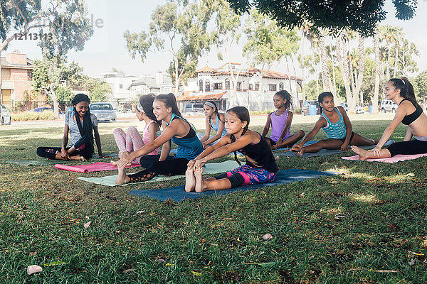 Schulmädchen üben Yoga  indem sie die Zehen auf dem Schulsportplatz berühren