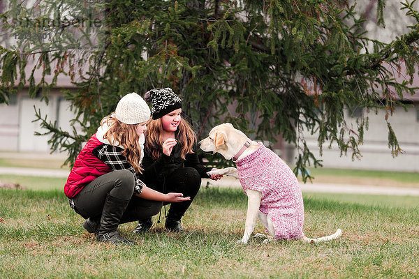 Mädchen und ihre Schwester kauern  um im Garten eine Hundepfote zu halten