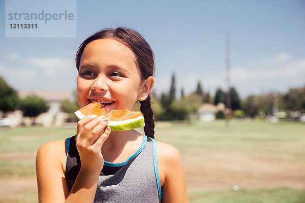 Schulmädchen isst Melonenscheibe auf Schulsportplatz