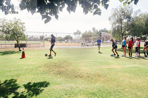 Männlicher Lehrer übt mit Schulmädchen auf dem Schulsportplatz Fussball