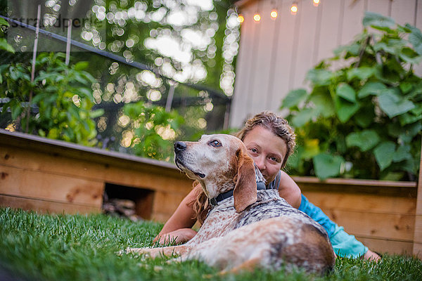 Porträt einer reifen Frau und eines Hundes  die zusammen auf dem Gartenrasen liegen