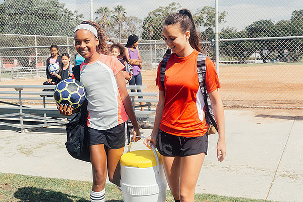 Schulmädchen tragen Kühlbox zum Fußballtraining auf dem Schulsportplatz