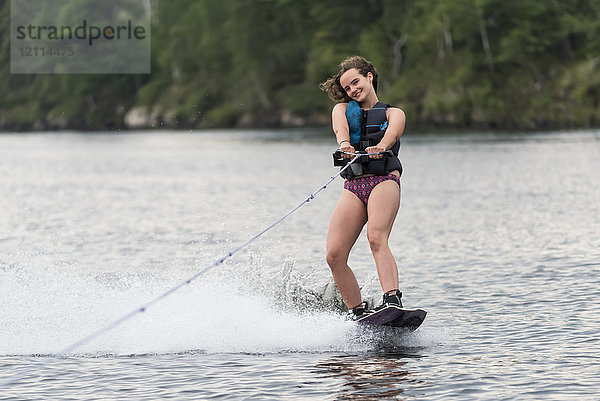 Ein jugendliches Mädchen  das hinter einem Boot auf einem See Wakeboard fährt; Lake of the Woods  Ontario  Kanada