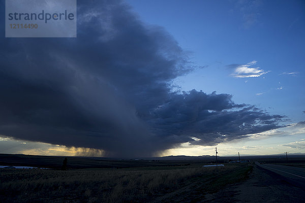 Dramatische Gewitterwolken und fallender Regen am Horizont  der bei Sonnenuntergang im Sonnenlicht glüht; Idaho  Vereinigte Staaten von Amerika