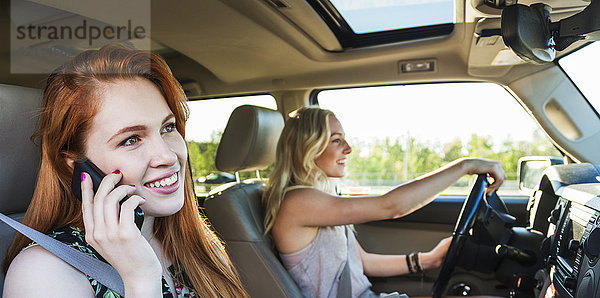 Zwei junge Frauen  die in einem Auto unterwegs sind  während die eine mit einem Smartphone telefoniert; Edmonton  Alberta  Kanada