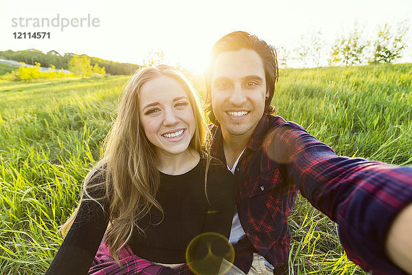 Junges Paar in einem Park  das für ein Selbstporträt mit seinem Mobiltelefon posiert; Edmonton  Alberta  Kanada