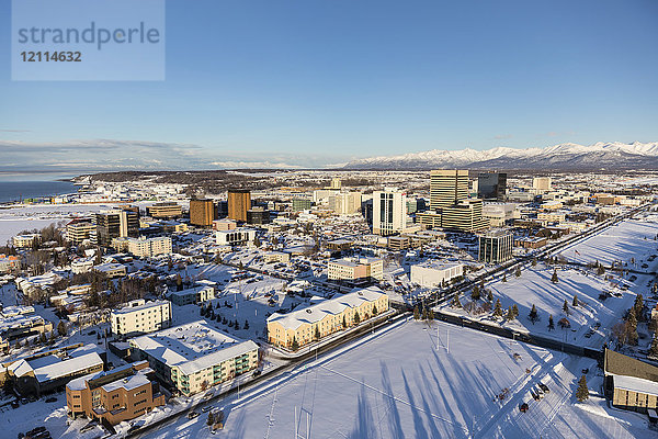 Luftaufnahme der schneebedeckten Innenstadt von Anchorage und der Chugach- und Talkeetna-Berge  die sich hinter der Stadt in der Ferne erstrecken  im Vordergrund ist der Park Strip zu sehen  Süd-Zentral-Alaska im Winter; Anchorage  Alaska  Vereinigte Staaten von Amerika