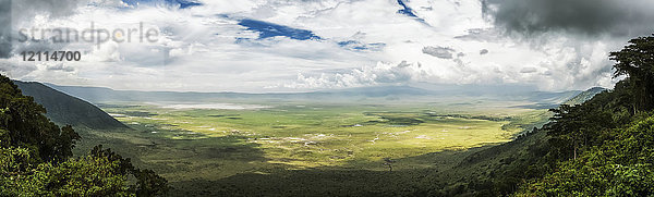 Wolken füllen den Himmel und werfen Schatten in das grüne Tal  das von Bergen umgeben ist; Tansania