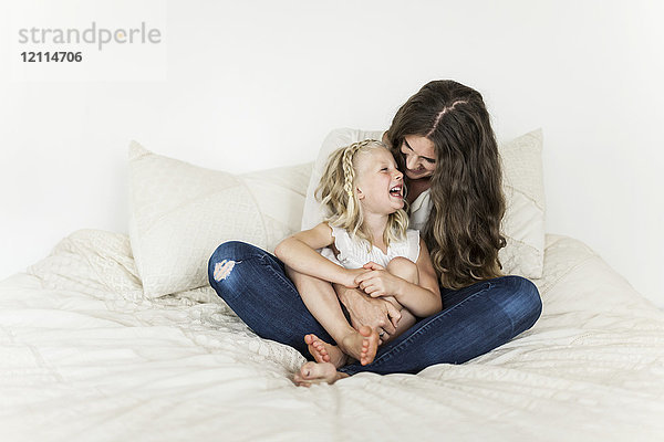 Porträt einer Mutter und ihrer kleinen Tochter  die auf einem Bett sitzen und Zeit miteinander verbringen und lachen; Sorrento  British Columbia  Kanada