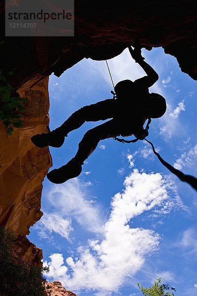 Blick nach oben auf die Silhouette eines Abenteurers  der sich an einer Schlucht in der Wüste abseilt; Hanksville  Utah  Vereinigte Staaten von Amerika