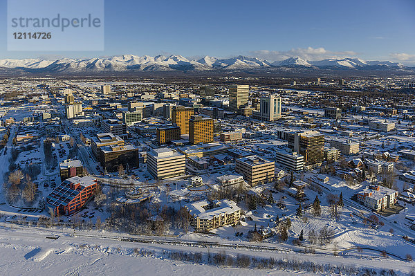 Luftaufnahme der schneebedeckten Innenstadt von Anchorage und der Chugach Mountains in der Ferne  das Capitan Cook Hotel und die Conoco Philips Gebäude im Vordergrund  Süd-Zentral-Alaska im Winter; Anchorage  Alaska  Vereinigte Staaten von Amerika