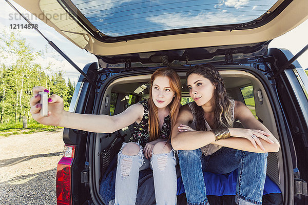 Zwei junge Frauen auf einer Autoreise sitzen auf dem Rücksitz eines Fahrzeugs und machen ein Selbstporträt mit einem Smartphone; Edmonton  Alberta  Kanada