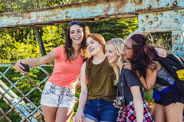 Eine Gruppe von vier Freundinnen posiert für ein Selbstporträt mit einem Smartphone auf einer Brücke in einem Park; Edmonton  Alberta  Kanada
