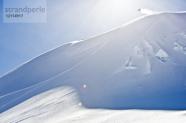 Ein professioneller Freeride-Snowboarder in der Luft auf einer verschneiten Piste vor einem blauen Himmel; British Columbia  Kanada