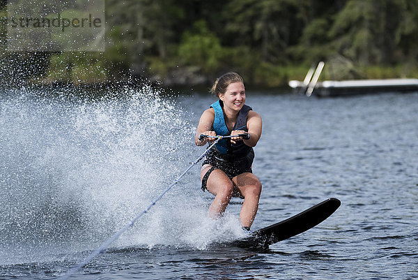 Eine junge Frau fährt Wakeboard hinter einem Boot auf einem See; Lake of the Woods  Ontario  Kanada