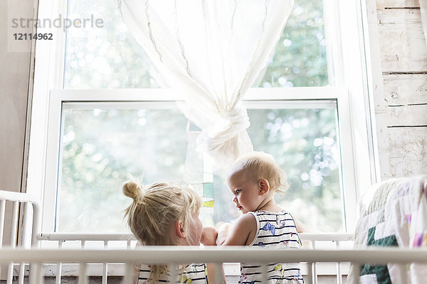 Zwei Schwestern  ein Baby und ein Kleinkind  spielen zusammen in einem Kinderbett an einem Fenster; Sorrento  British Columbia  Kanada