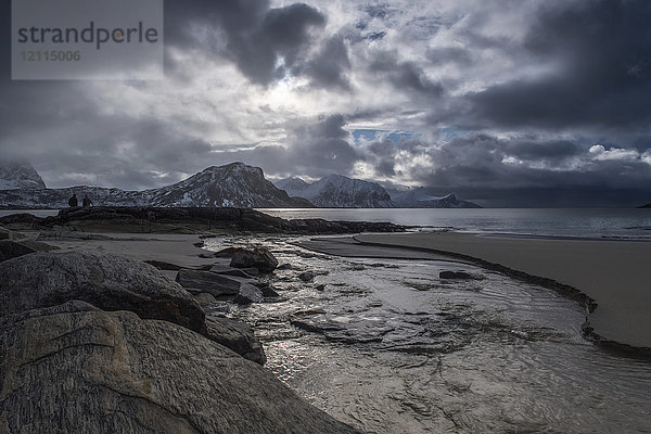 Eine Landschaft mit zerklüfteten Bergen und Sand entlang der Küstenlinie unter einem bewölkten Himmel; Nordland  Norwegen