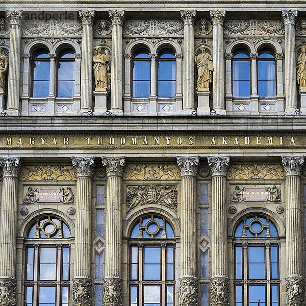Verschnörkelte Fassade eines Gebäudes mit Säulen und Statuen neben den Fenstern mit Reflexion des blauen Himmels; Budapest  Budapest  Ungarn